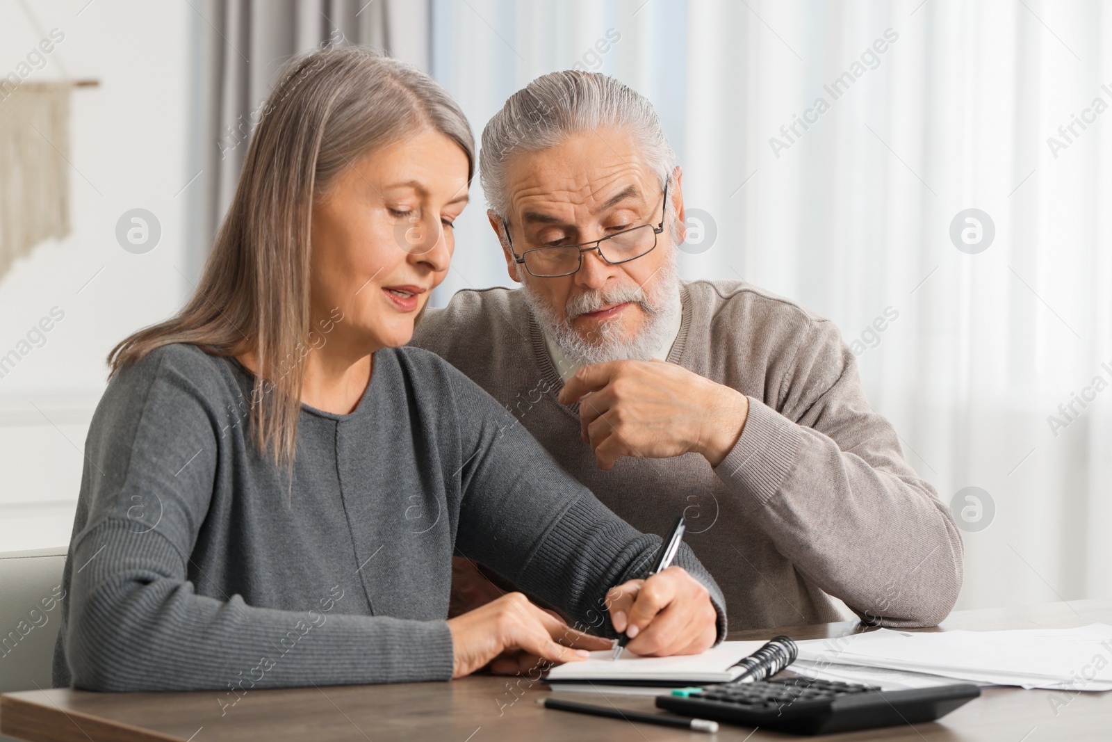 Photo of Elderly couple with papers discussing pension plan at wooden table indoors