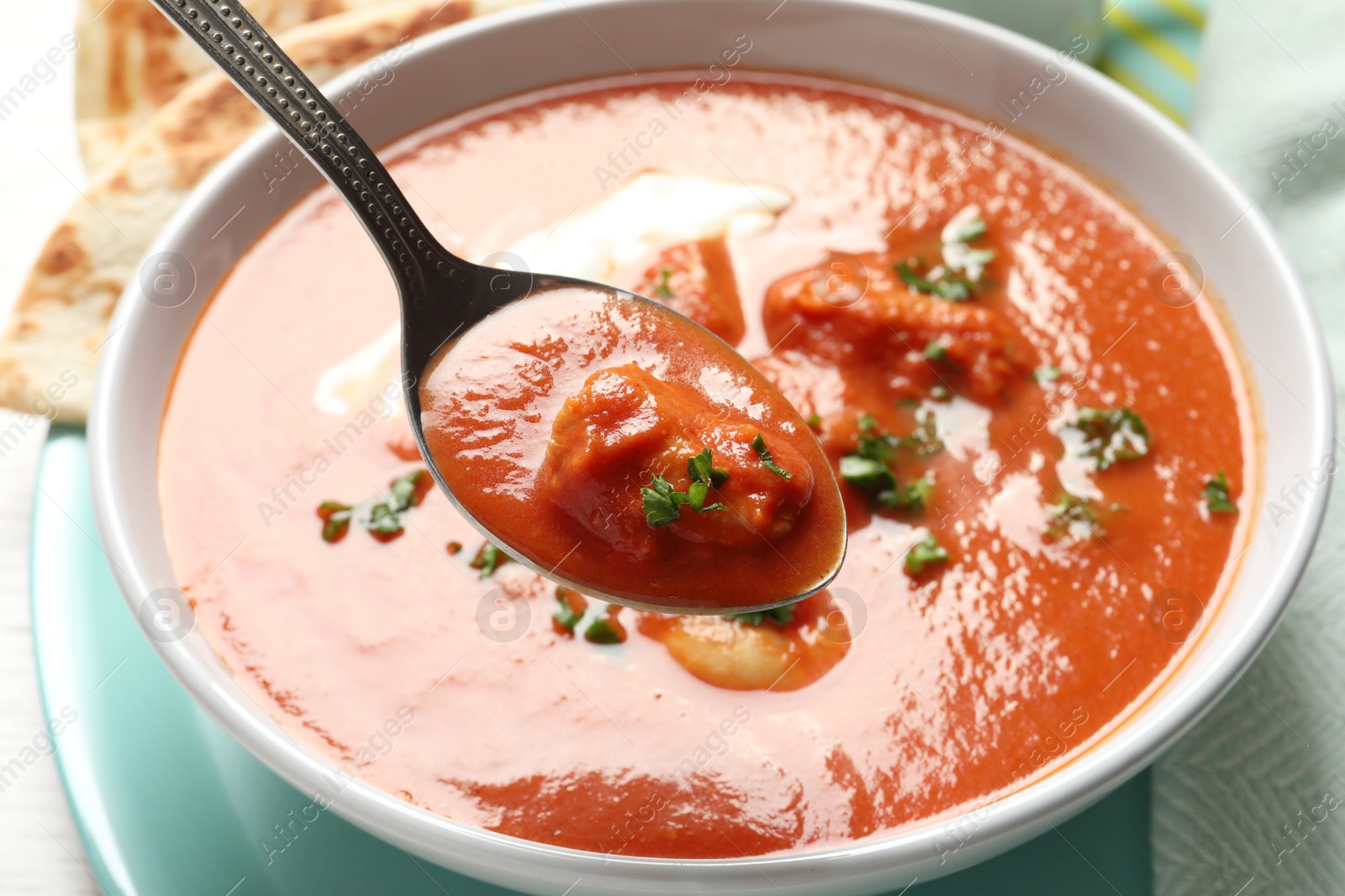 Photo of Spoon with tasty butter chicken over bowl of meal, closeup. Traditional Murgh Makhani dish