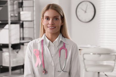 Photo of Doctor with stethoscope and pink ribbon indoors, space for text. Breast cancer awareness