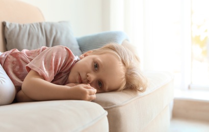 Photo of Cute little girl lying on sofa in room