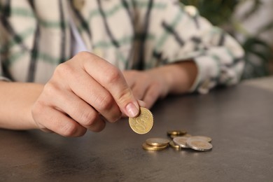 Photo of Poor woman counting coins at grey table indoors, closeup