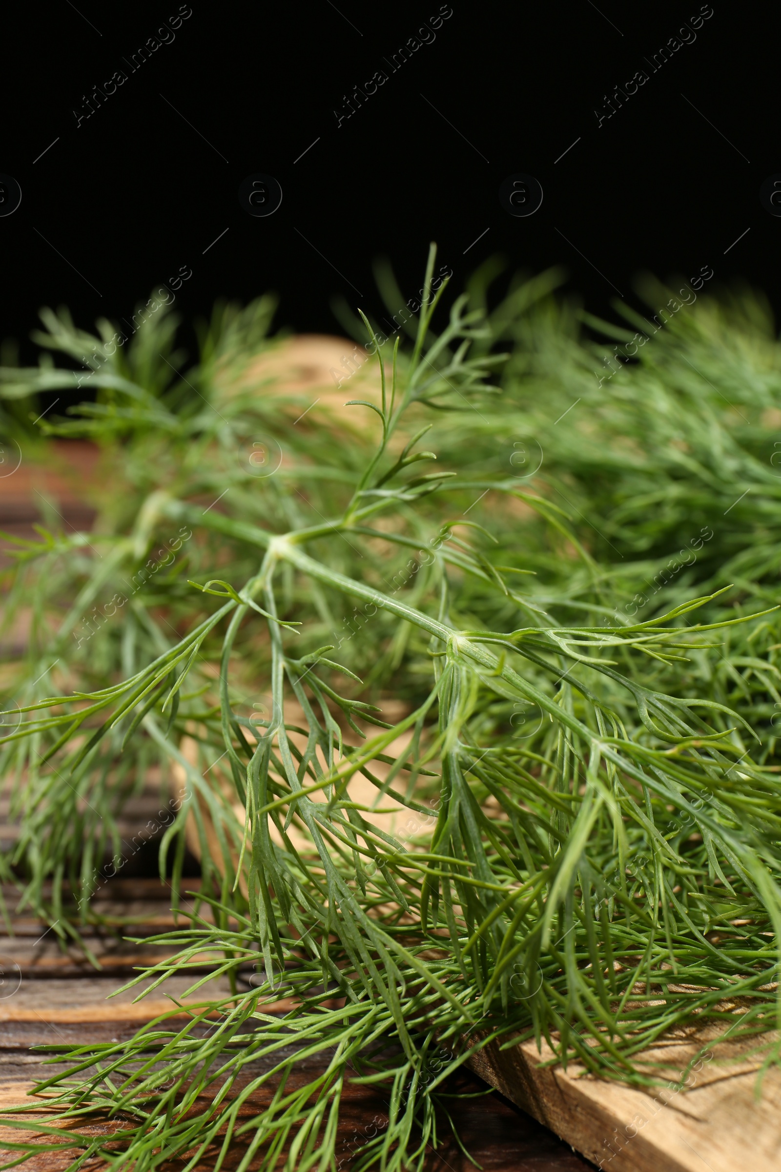 Photo of Board with fresh green dill on wooden table against black background, closeup