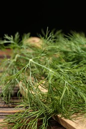 Photo of Board with fresh green dill on wooden table against black background, closeup