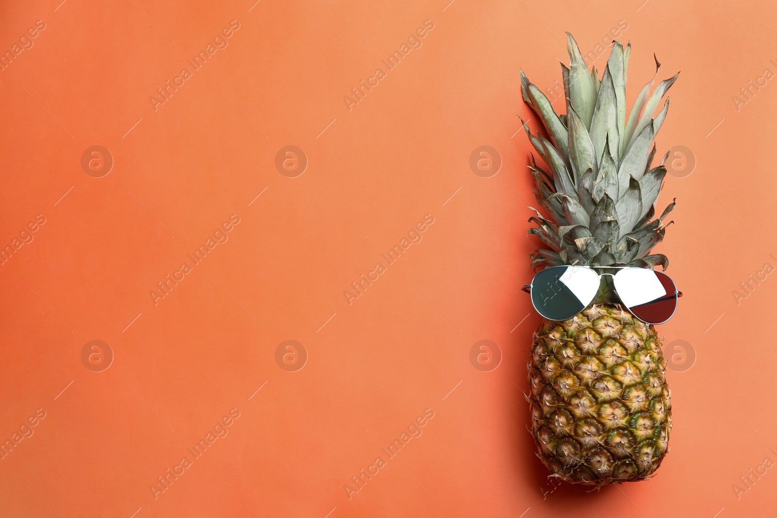 Photo of Top view of pineapple with sunglasses on orange background, space for text. Creative concept