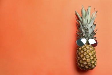 Top view of pineapple with sunglasses on orange background, space for text. Creative concept
