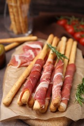 Delicious grissini sticks with prosciutto on table