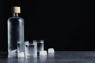 Photo of Bottle of vodka and shot glasses with ice on dark table against black background. Space for text