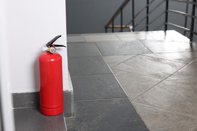 Red fire extinguisher near white wall, space for text