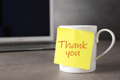 Mug and sticky note with phrase Thank You on grey table. Space for text