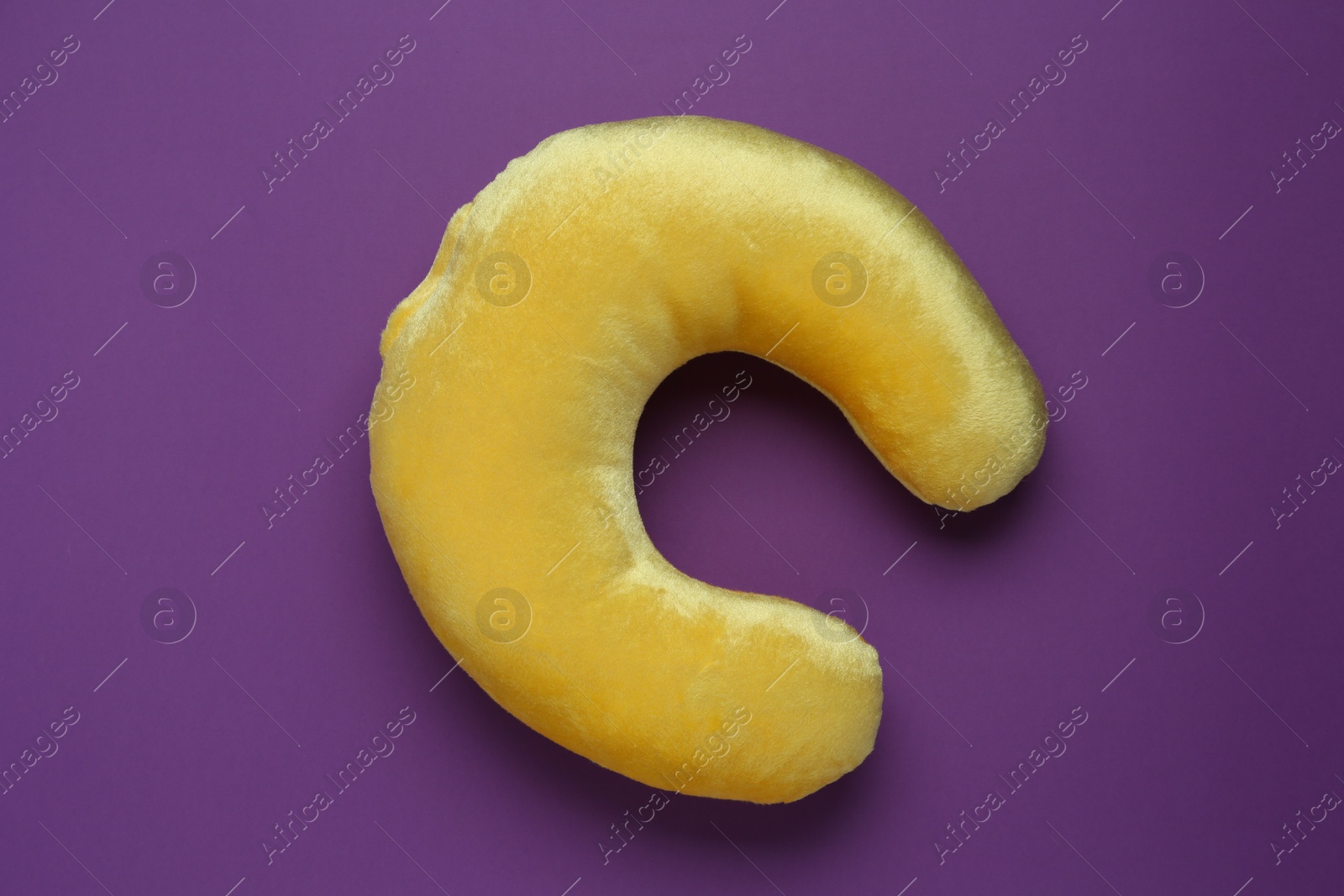 Photo of Yellow travel pillow on purple background, top view