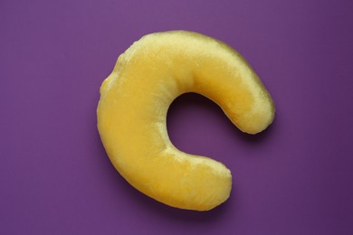 Yellow travel pillow on purple background, top view