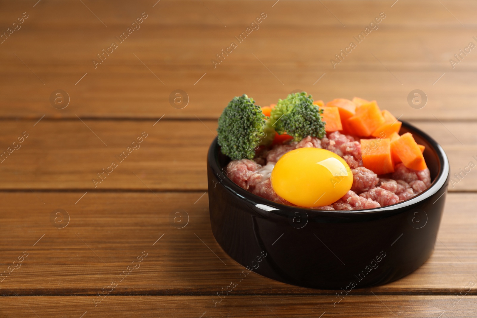 Photo of Natural pet food in feeding bowl on wooden table, closeup. Space for text