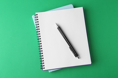 Photo of Notebooks and pen on green background, top view