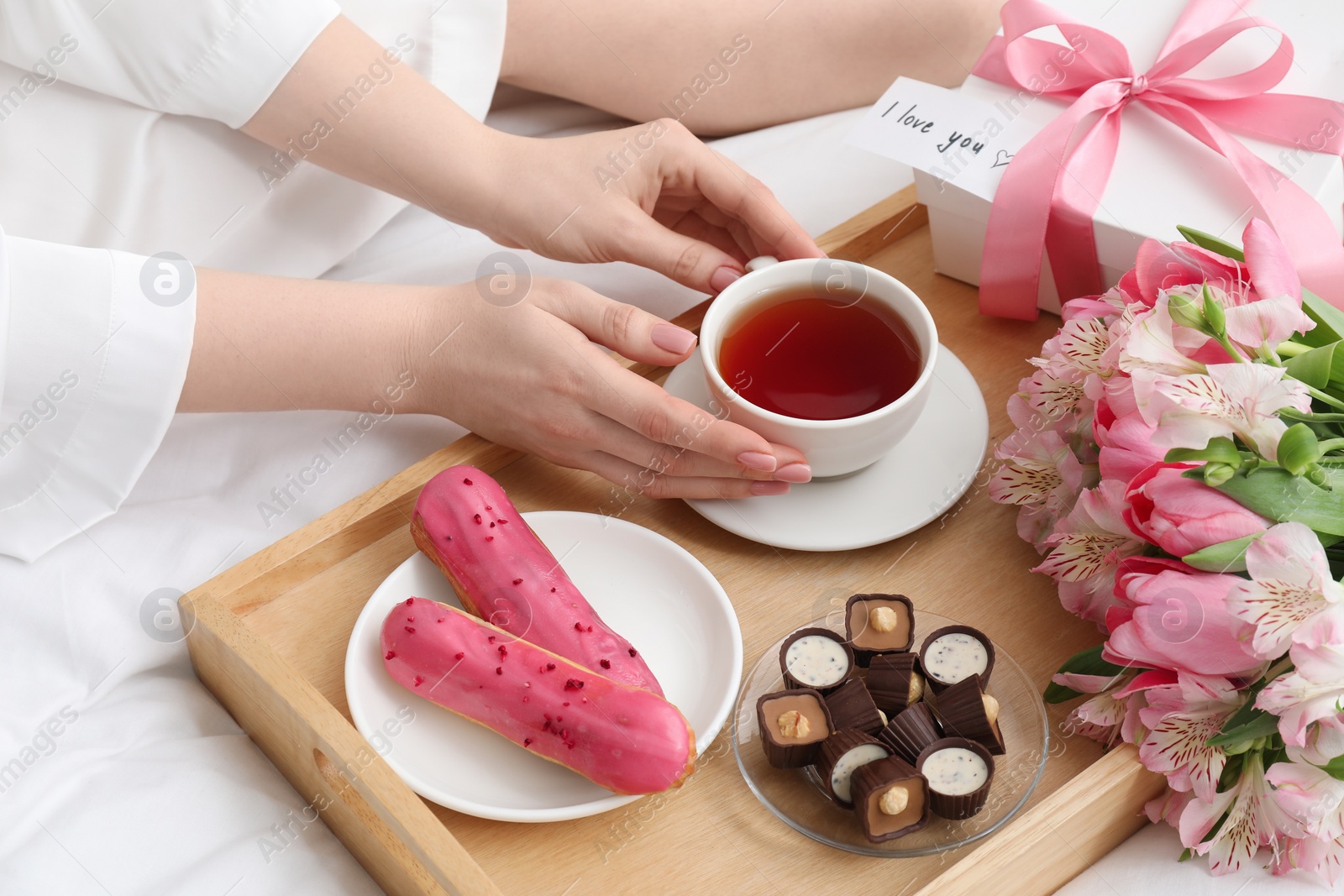 Photo of Tasty breakfast served in bed. Woman with tea, desserts, gift box, flowers and I Love You card at home, closeup