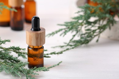 Bottle of juniper essential oil and twigs on white wooden table. Space for text