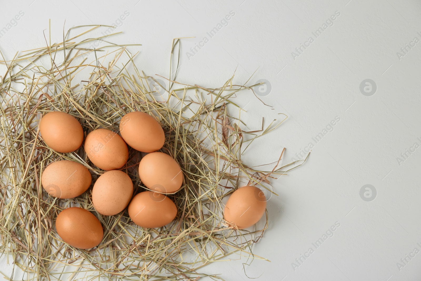 Photo of Raw chicken eggs and decorative straw on white table, flat lay. Space for text