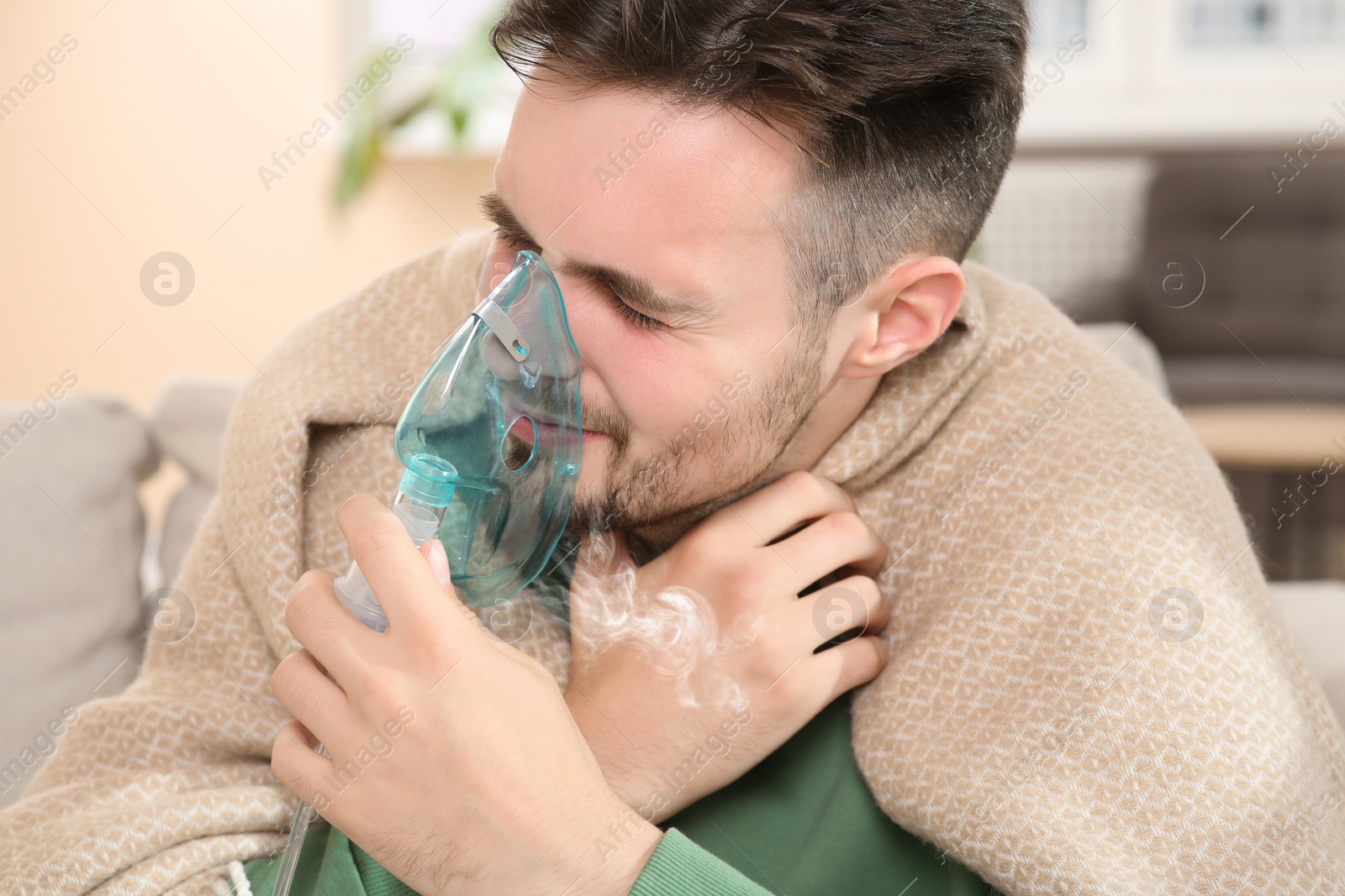 Photo of Sick man using nebulizer for inhalation indoors