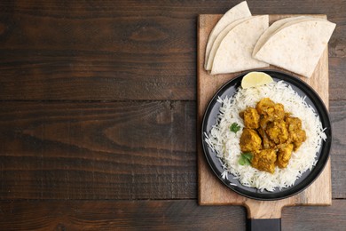 Photo of Delicious chicken curry with rice and tortillas on wooden table, top view. Space for text