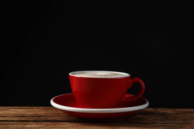 Red cup with aromatic cappuccino on wooden table against black background