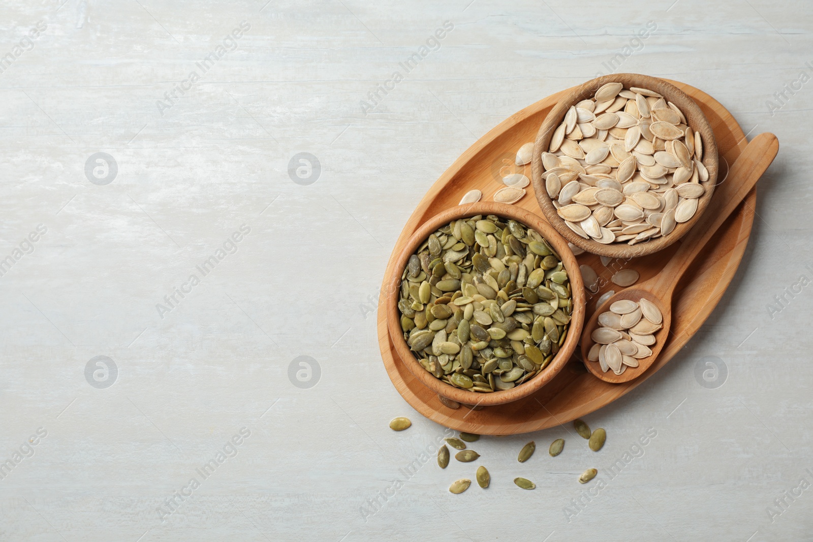 Photo of Raw pumpkin seeds in dish on light background, top view. Space for text