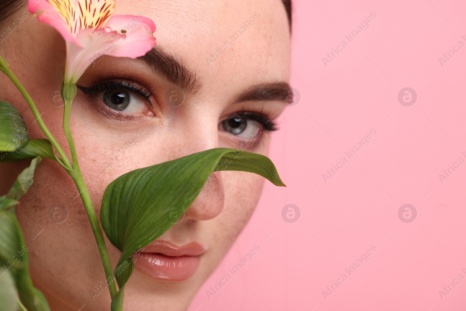 Photo of Beautiful woman with fake freckles and flower on pink background, closeup. Space for text