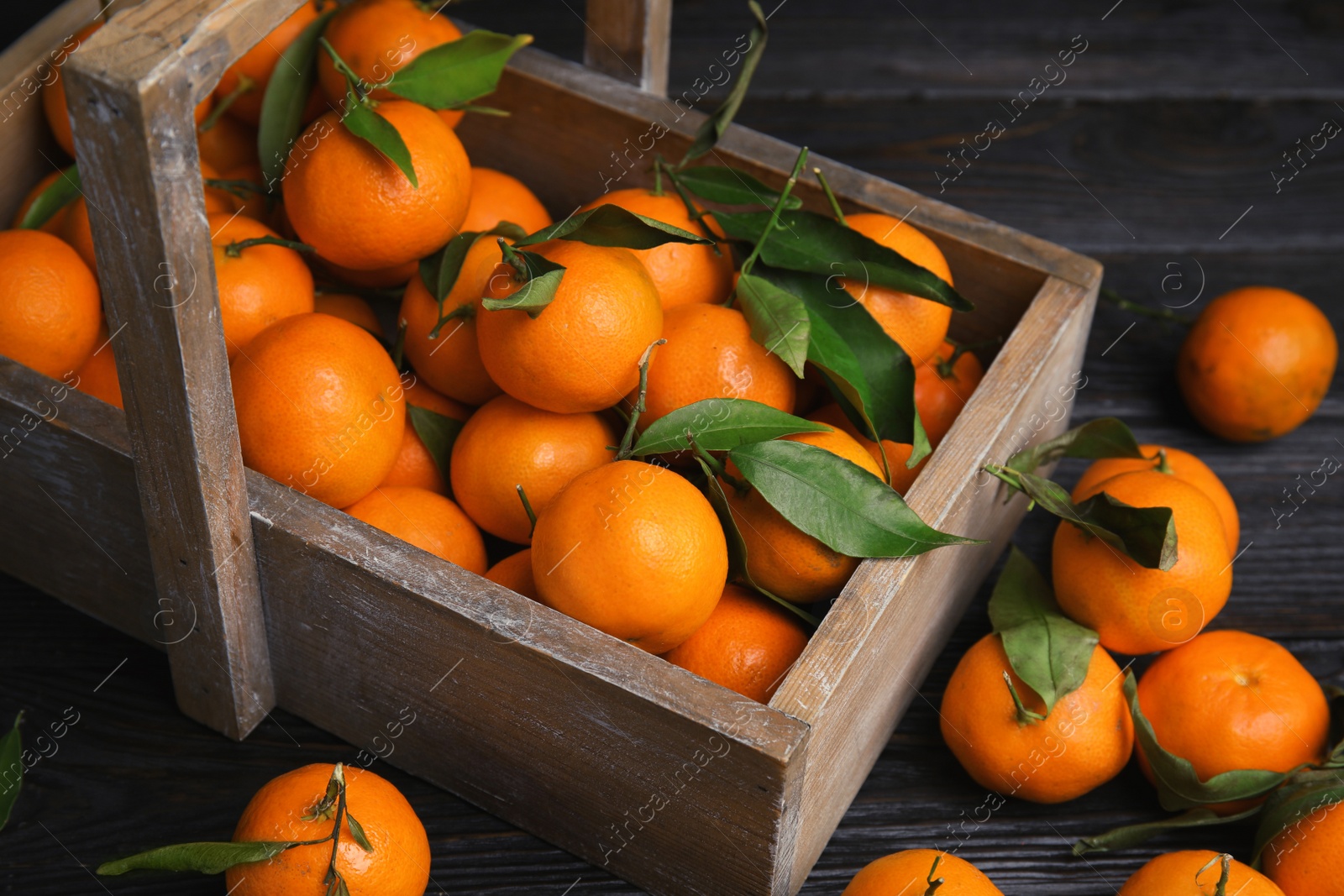 Photo of Fresh ripe tangerines with green leaves and wooden basket on table