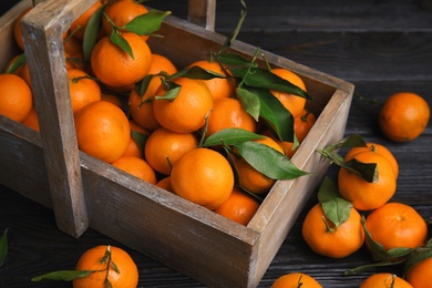 Fresh ripe tangerines with green leaves and wooden basket on table