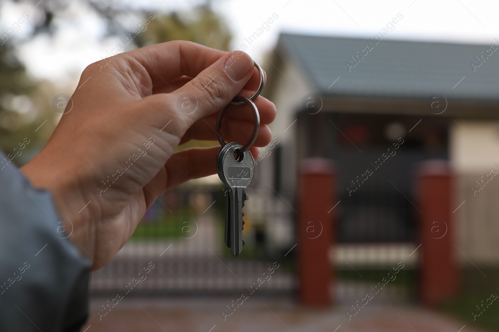 Photo of Real estate agent holding keys to new house outdoors, closeup. Space for text