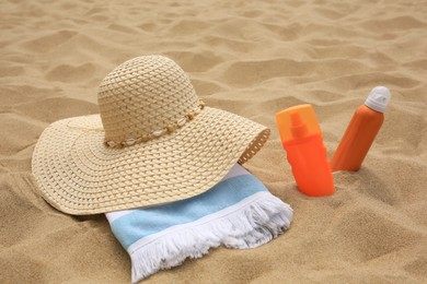 Photo of Sunscreens, hat and towel on sand. Sun protection care