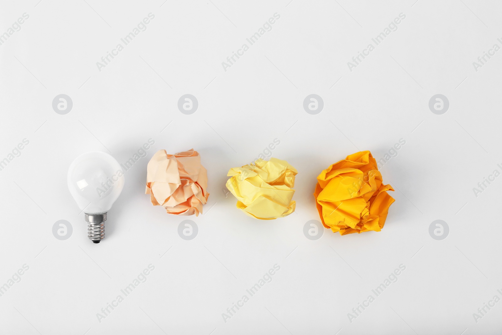 Photo of Composition with lamp bulb and crumpled paper balls on white background, top view. Creative concept