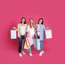 Happy pregnant women with shopping bags on pink background
