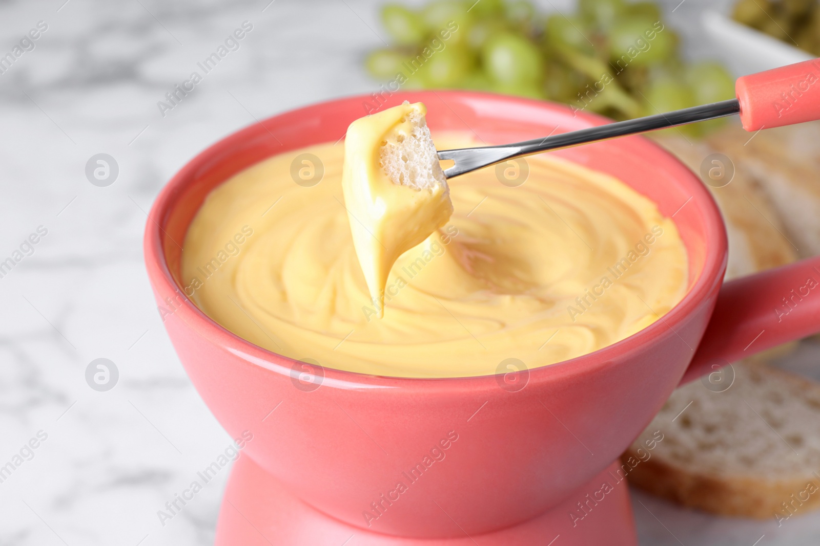 Photo of Dipping bread into pot with cheese fondue on table, closeup