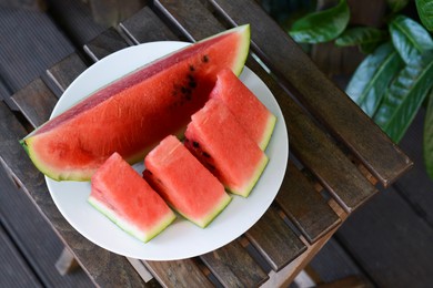 Photo of White plate with sliced watermelon on wooden stool outdoors. Space for text