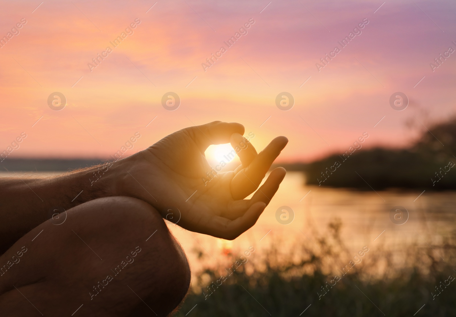 Image of Man meditating near river at sunset, closeup. Practicing yoga