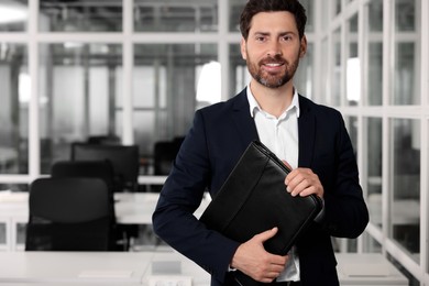 Photo of Happy real estate agent with leather portfolio indoors. Space for text