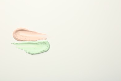 Photo of Strokes of pink and green color correcting concealers on white background, top view