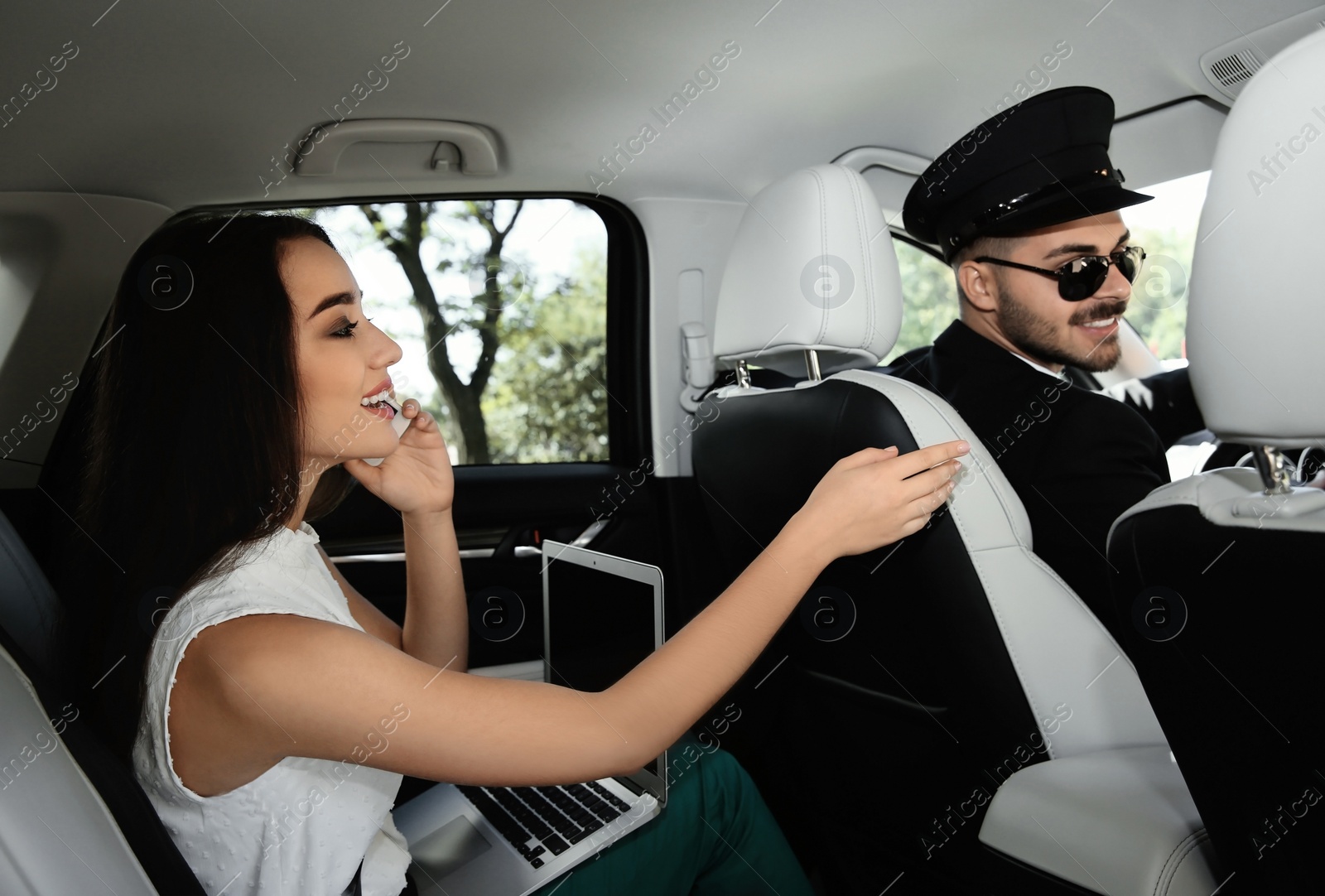Photo of Young businesswoman talking on phone and driver in luxury car