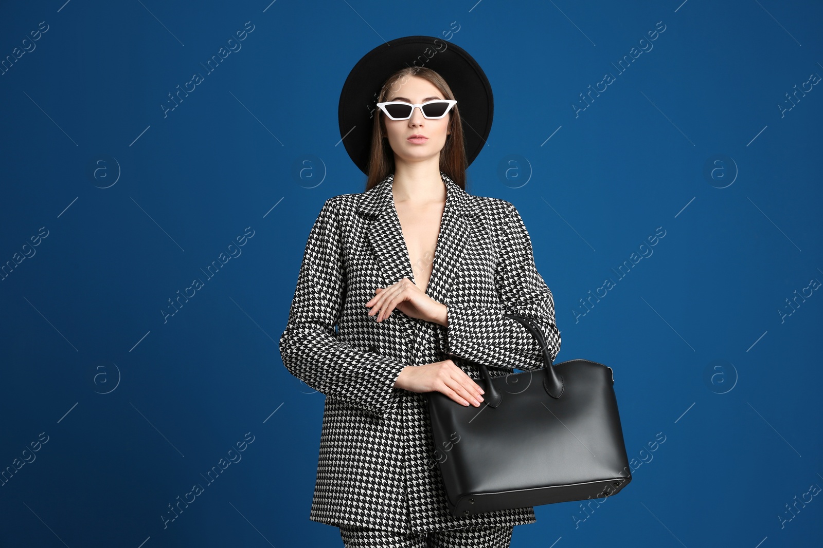 Photo of Beautiful young woman in sunglasses with stylish bag on blue background