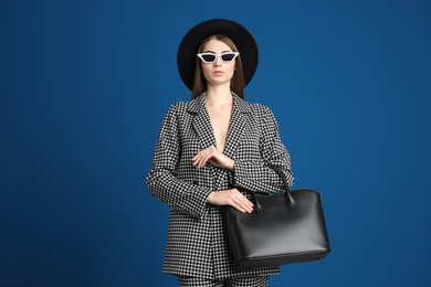 Beautiful young woman in sunglasses with stylish bag on blue background