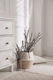 Photo of Pussy willow tree branches and pillow near chest of drawers in room