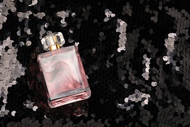 Photo of Luxury perfume in bottle on fabric with shiny sequins, above view