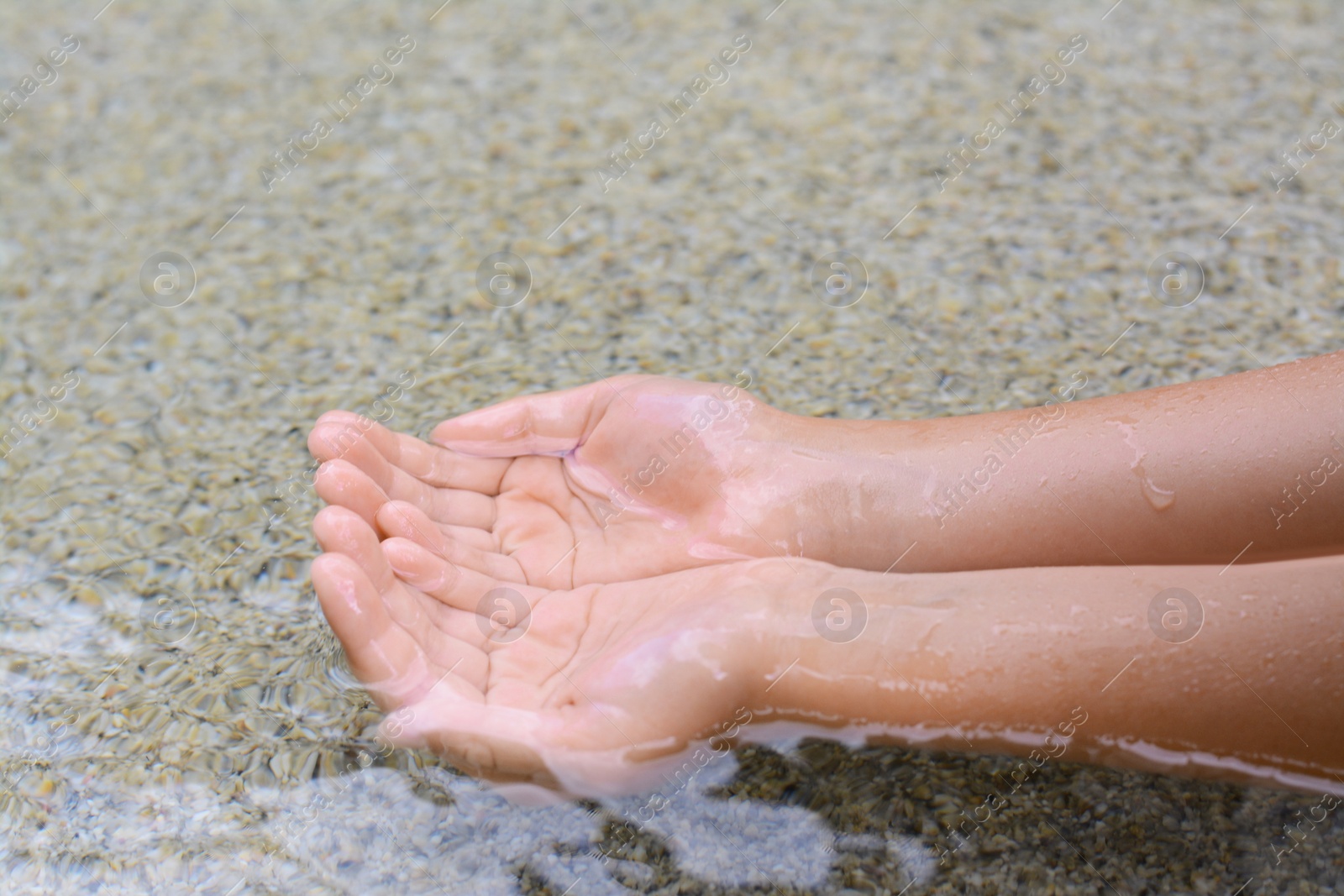 Photo of Kid dipping hands in water outdoors, closeup