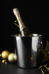 Photo of Happy New Year! Bottle of sparkling wine in bucket and festive decor on table against black background