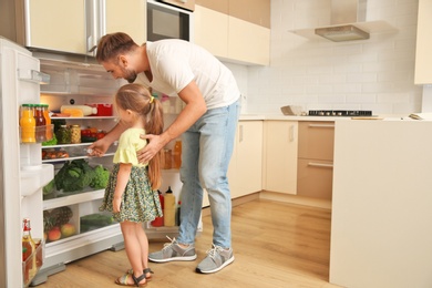 Young father and daughter choosing food in refrigerator at kitchen