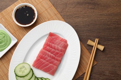 Tasty sashimi (pieces of fresh raw tuna), cucumber slices, soy sauce and wasabi on wooden table, flat lay