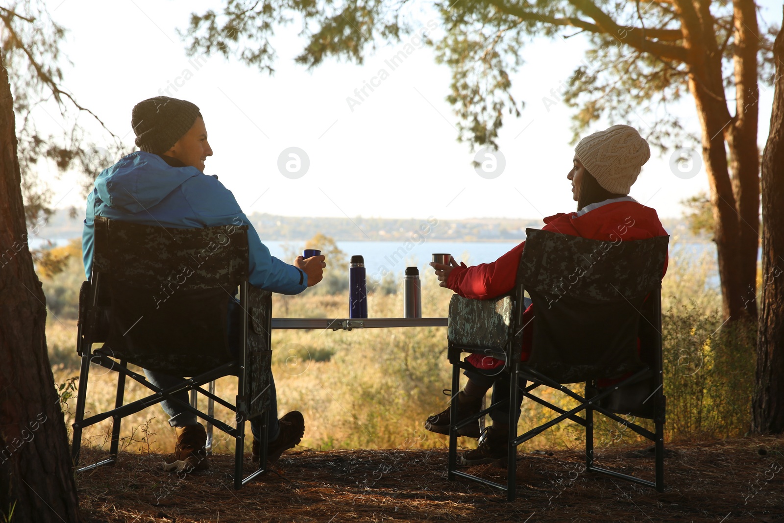 Photo of Couple resting in camping chairs and enjoying hot drink outdoors