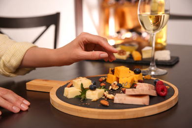 Woman with different types of delicious cheeses at table indoors, closeup