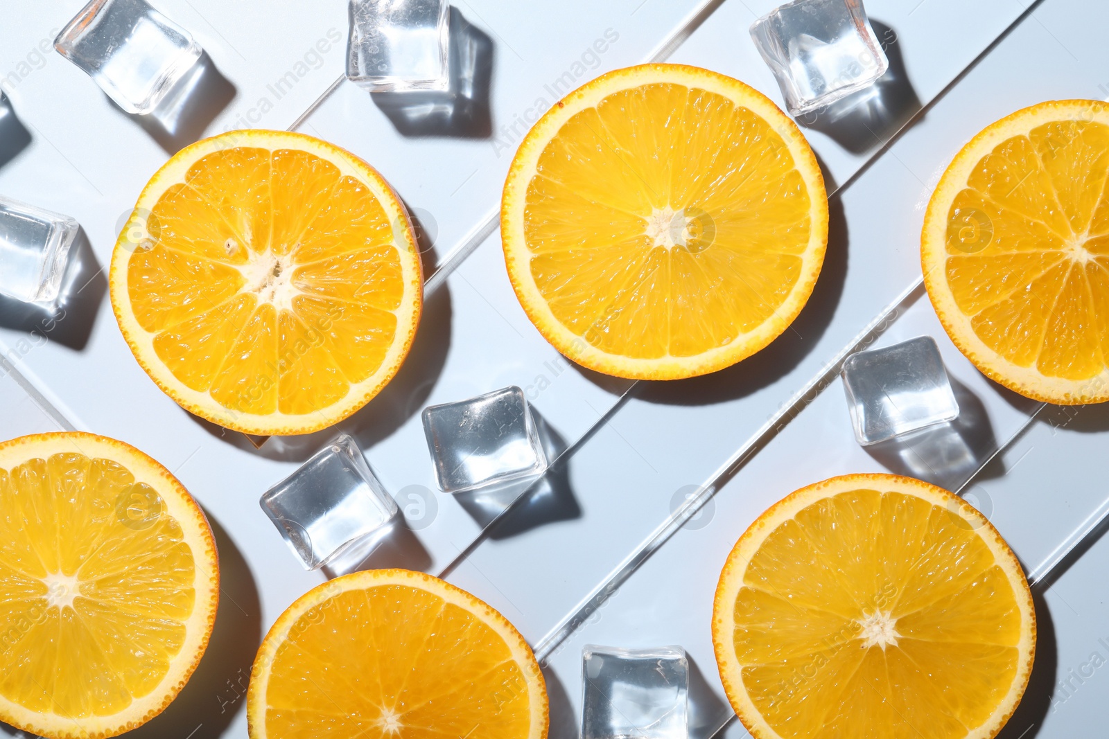 Photo of Slices of juicy orange and ice cubes on light blue background, flat lay