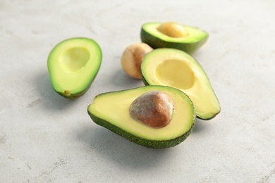 Tasty ripe avocados cut into halves on light background