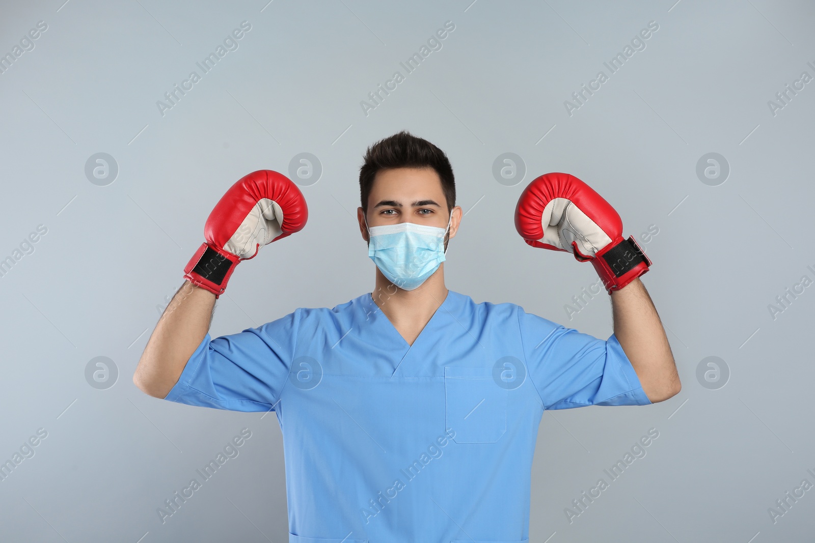 Photo of Doctor with protective mask and boxing gloves on light grey background. Strong immunity concept